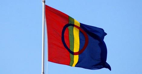 Bildet viser det samiske flagget som vaier i vinden mot blå himmel